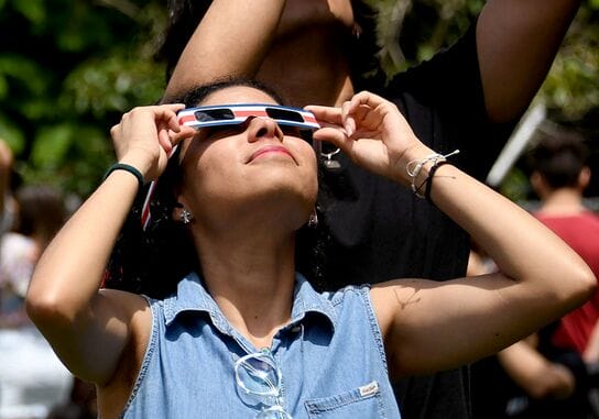 Vrouw die veilig naar een zonsverduistering kijkt via een gecertificeerde eclipsbril buitenshuis